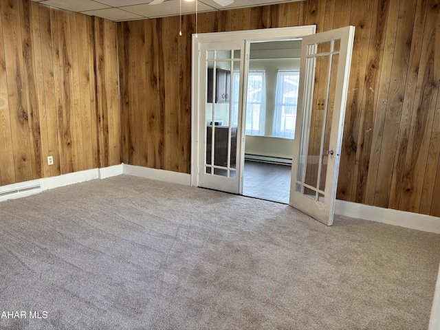 unfurnished room featuring carpet flooring, ceiling fan, french doors, baseboard heating, and wood walls