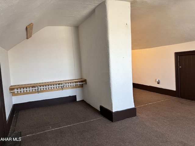 hall with dark carpet, lofted ceiling, and a textured ceiling