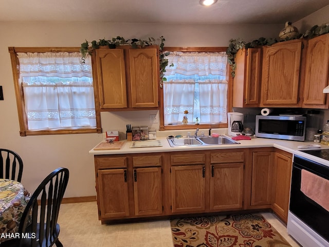 kitchen with electric range, brown cabinets, a sink, stainless steel microwave, and light countertops