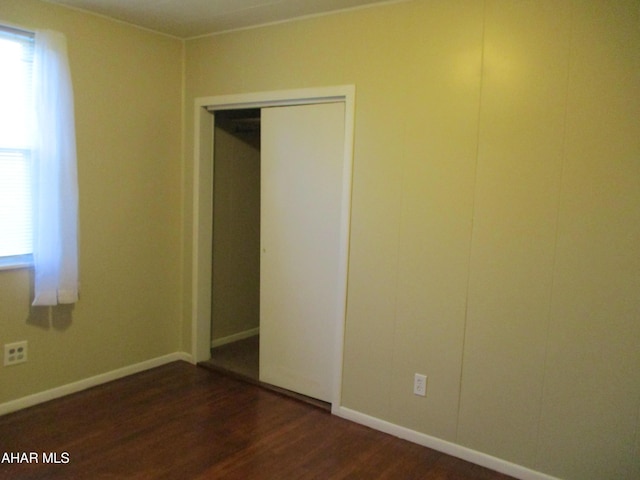 unfurnished bedroom with a closet, baseboards, and dark wood-type flooring