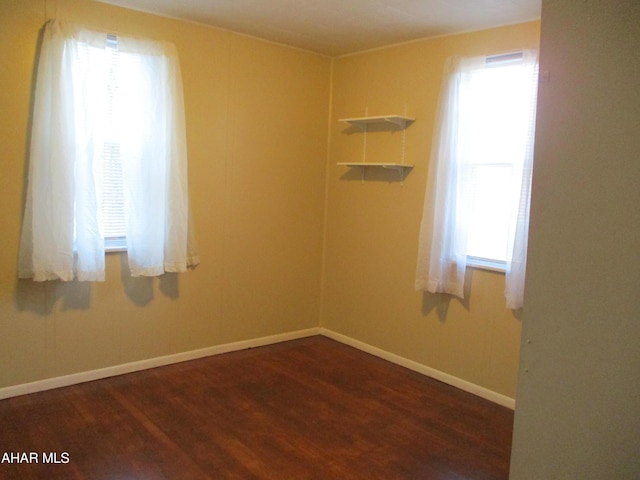 empty room with plenty of natural light, wood finished floors, and baseboards