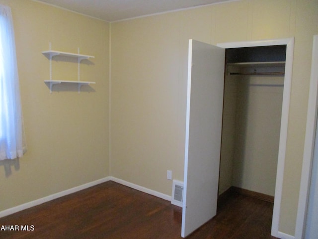 unfurnished bedroom featuring visible vents, dark wood-style flooring, a closet, and baseboards