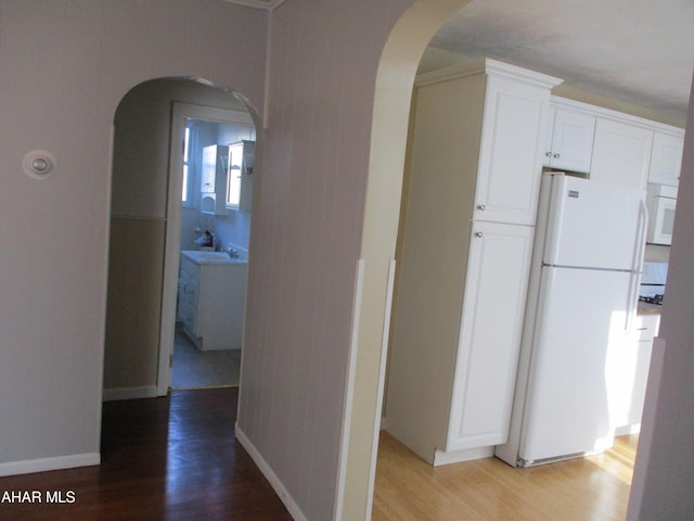 hallway featuring light wood-type flooring, arched walkways, and baseboards