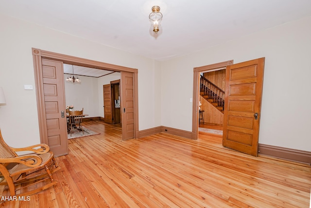 spare room featuring a chandelier, light wood-style floors, baseboards, and stairs
