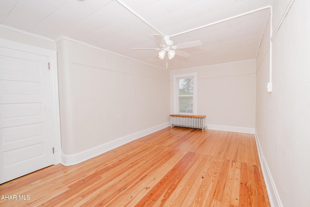 empty room with radiator, crown molding, wood-type flooring, a ceiling fan, and baseboards