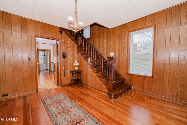 stairway with hardwood / wood-style floors, a chandelier, and wood walls