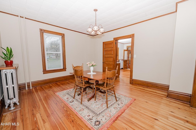 dining space featuring light wood-type flooring, baseboards, a chandelier, radiator, and ornamental molding