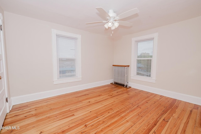 spare room with baseboards, light wood-type flooring, a ceiling fan, and radiator
