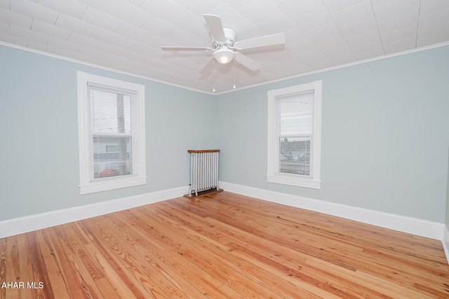 empty room featuring ornamental molding, healthy amount of natural light, hardwood / wood-style flooring, baseboards, and a ceiling fan