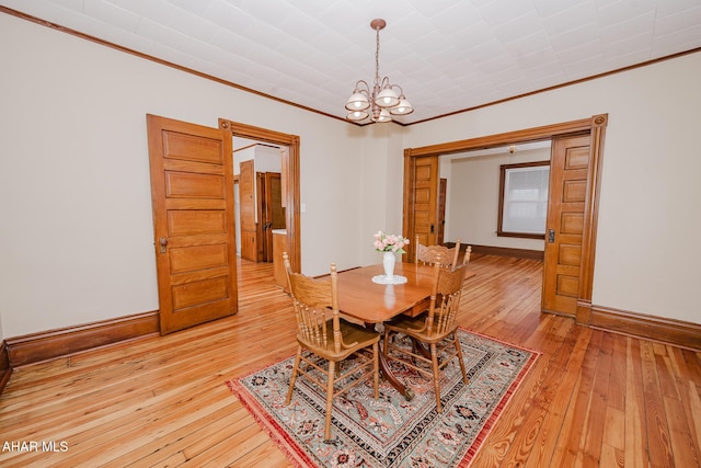 dining area with a chandelier, ornamental molding, light wood-style flooring, and baseboards
