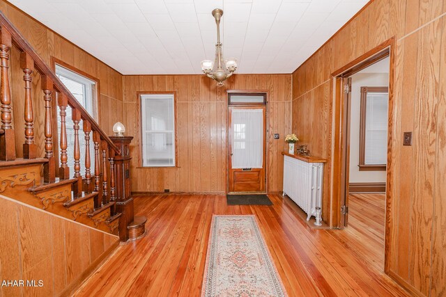 entryway featuring wood-type flooring, plenty of natural light, a chandelier, radiator, and wood walls