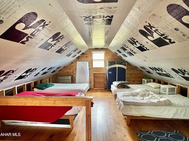 bedroom featuring hardwood / wood-style floors, wooden walls, and vaulted ceiling