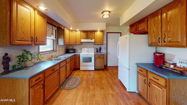 kitchen with under cabinet range hood, white appliances, brown cabinetry, and a sink