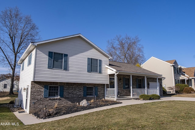 tri-level home with brick siding, a porch, a front yard, a garage, and driveway