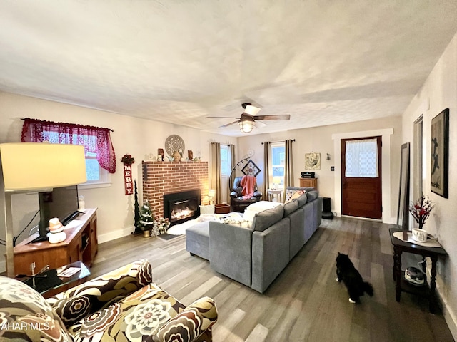 living room featuring hardwood / wood-style flooring, ceiling fan, and a brick fireplace