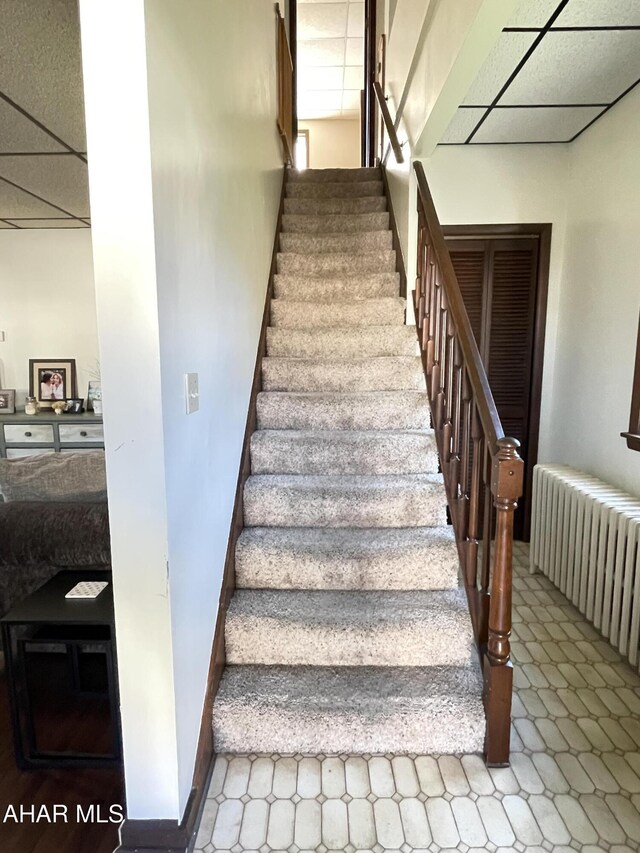 staircase featuring radiator and a drop ceiling