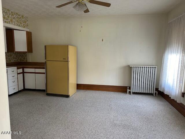 kitchen featuring radiator, ceiling fan, a textured ceiling, white fridge, and light colored carpet