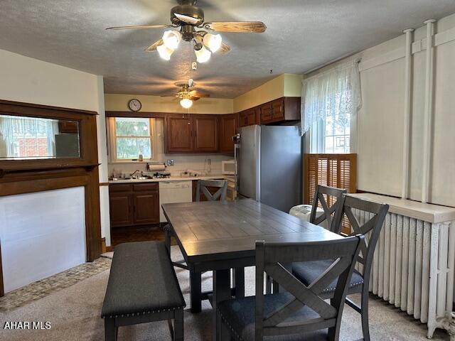 carpeted dining space featuring radiator heating unit, a textured ceiling, ceiling fan, and sink