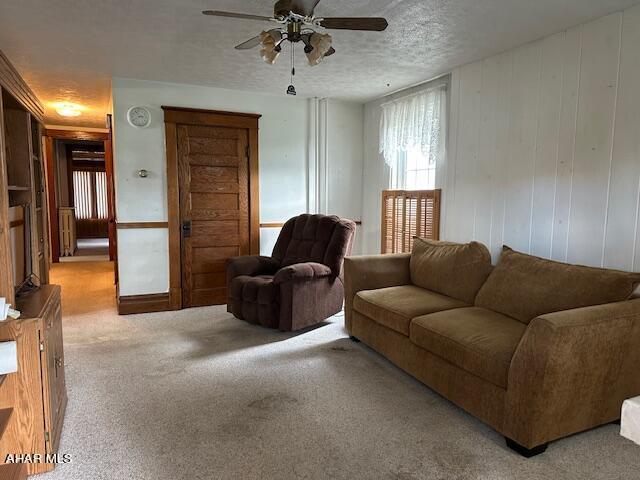 carpeted living room featuring ceiling fan, wooden walls, and a textured ceiling