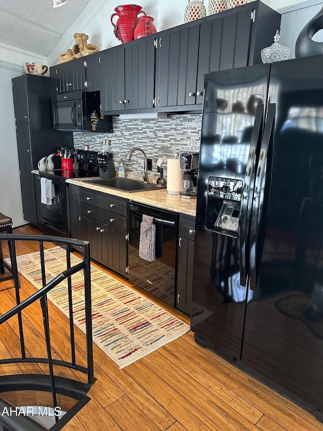 kitchen featuring black appliances, tasteful backsplash, sink, vaulted ceiling, and light hardwood / wood-style flooring