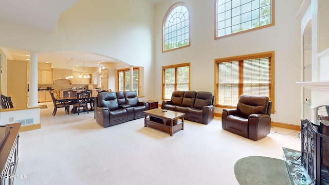 living room with ornate columns, a towering ceiling, arched walkways, and light colored carpet