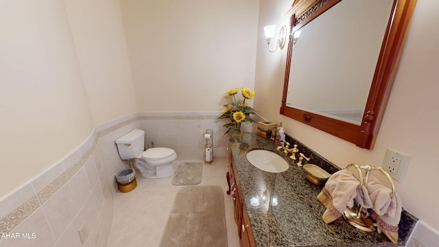 half bathroom featuring toilet, vanity, tile patterned floors, tile walls, and a wainscoted wall