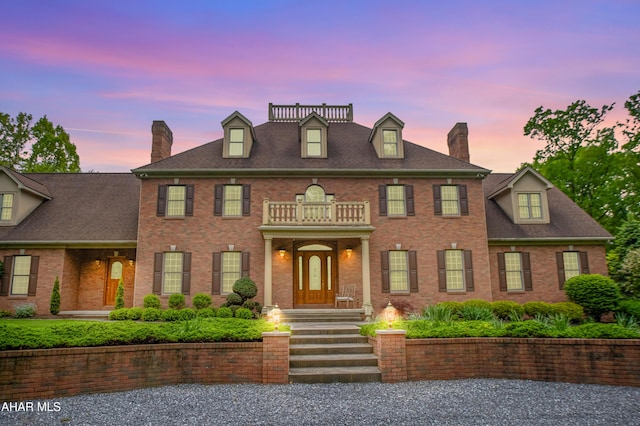 colonial-style house with a chimney, brick siding, and a balcony