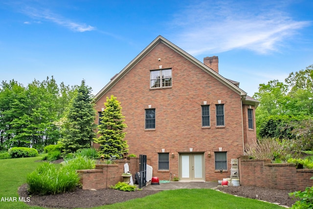 back of house with french doors, a chimney, a yard, and brick siding