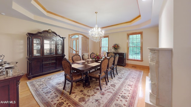 dining room with a tray ceiling, a chandelier, light wood finished floors, and arched walkways