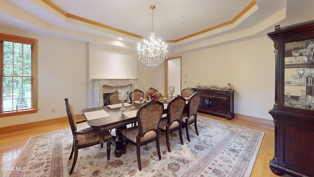 dining area featuring a tray ceiling, healthy amount of natural light, a chandelier, light wood-style flooring, and ornamental molding