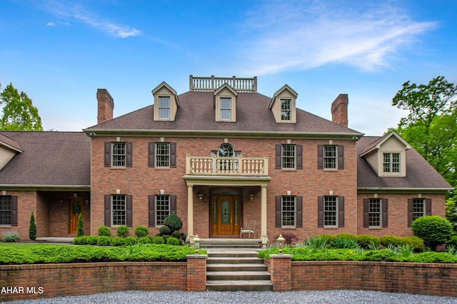colonial home featuring a balcony, a chimney, and brick siding