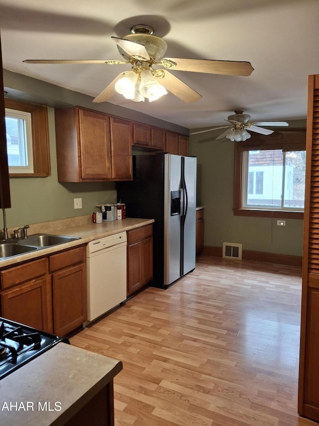 kitchen with a sink, visible vents, light countertops, dishwasher, and brown cabinetry