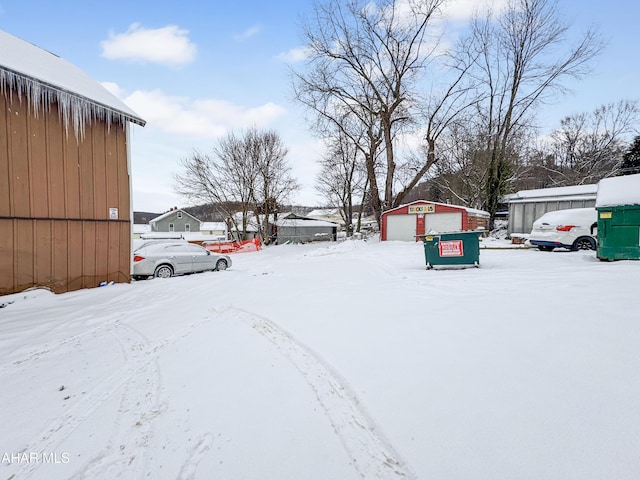 snowy yard with a garage and an outbuilding