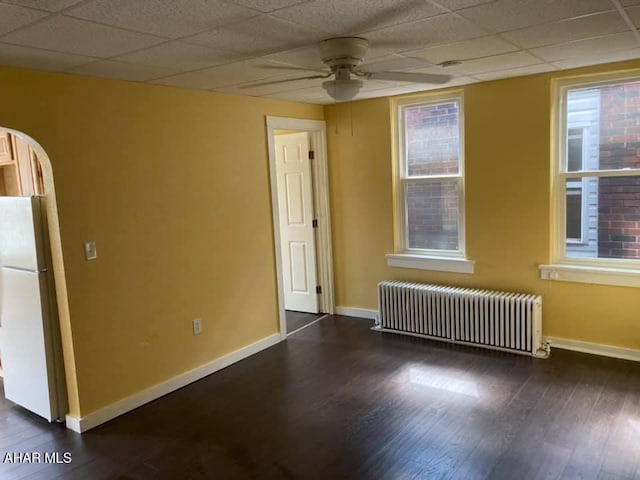 empty room featuring a paneled ceiling, ceiling fan, radiator heating unit, and dark wood-type flooring