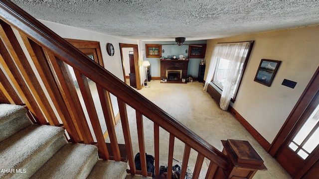 stairs featuring ceiling fan, a brick fireplace, carpet, and a textured ceiling