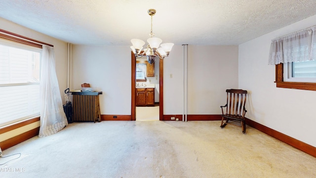 carpeted spare room featuring plenty of natural light, radiator, a textured ceiling, and a notable chandelier