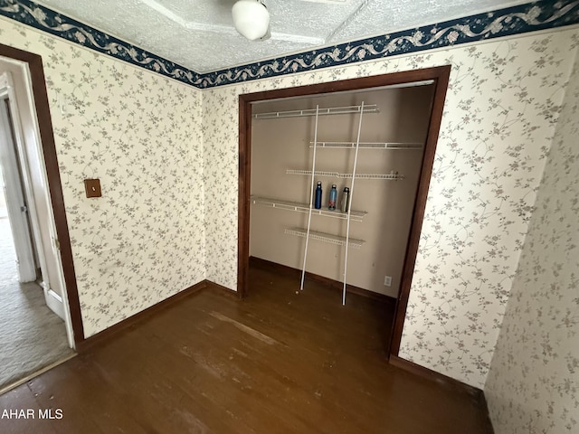unfurnished bedroom with wood finished floors, a closet, wallpapered walls, and baseboards