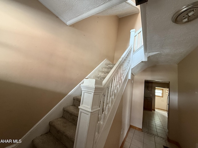 staircase with a textured ceiling, tile patterned floors, and baseboards
