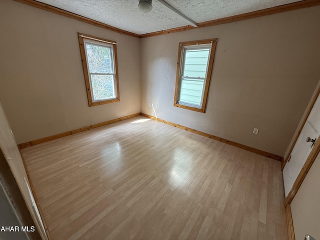 spare room with ornamental molding, baseboards, a textured ceiling, light wood finished floors, and ceiling fan