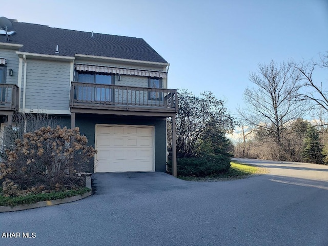 exterior space with driveway, a balcony, an attached garage, and a shingled roof