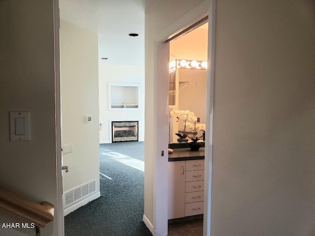 hall featuring heating unit, baseboards, visible vents, and dark carpet