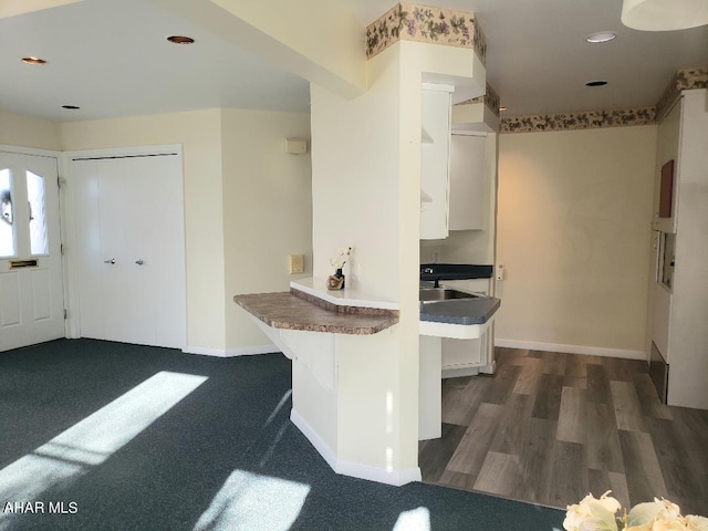 kitchen with baseboards, a breakfast bar, a peninsula, white cabinets, and a sink