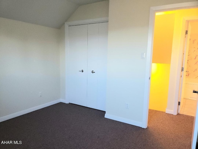 unfurnished bedroom featuring a closet, lofted ceiling, and dark colored carpet