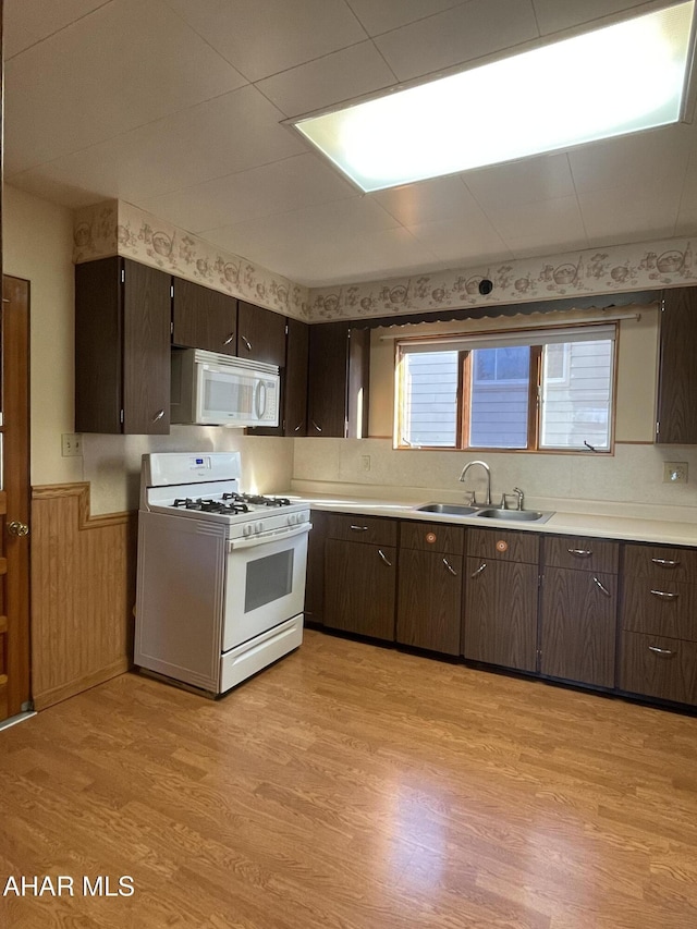 kitchen with dark brown cabinets, white appliances, sink, light hardwood / wood-style floors, and wood walls