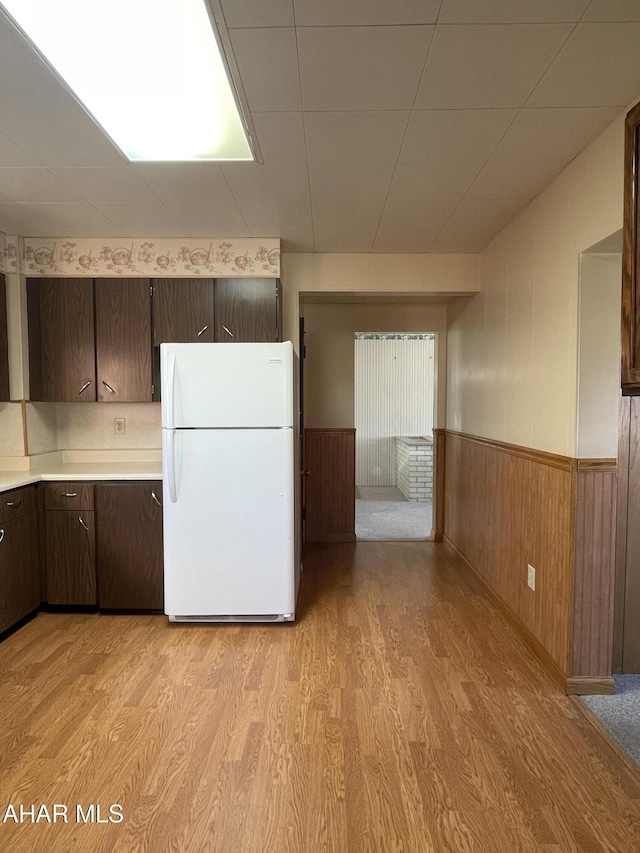 kitchen featuring wood walls, white fridge, dark brown cabinetry, and light hardwood / wood-style flooring