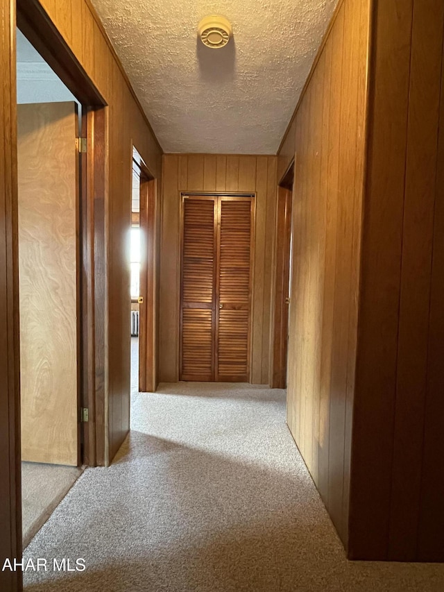 corridor with light carpet, a textured ceiling, and wooden walls