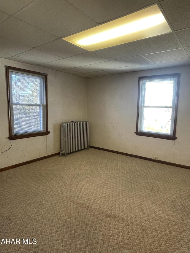 carpeted empty room with radiator and a paneled ceiling