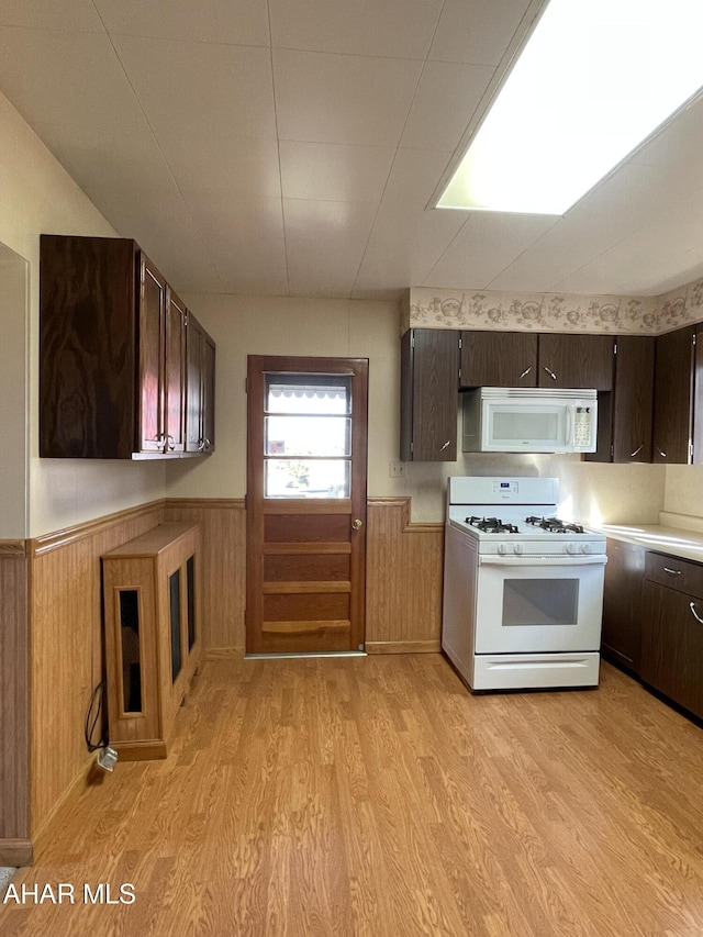 kitchen featuring light wood-type flooring, dark brown cabinets, white appliances, and wooden walls