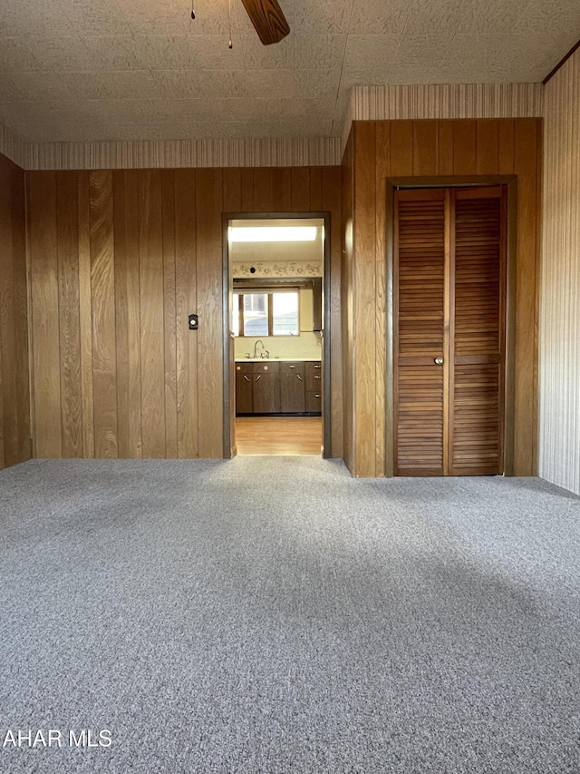 unfurnished bedroom with light colored carpet, ceiling fan, wooden walls, connected bathroom, and a closet