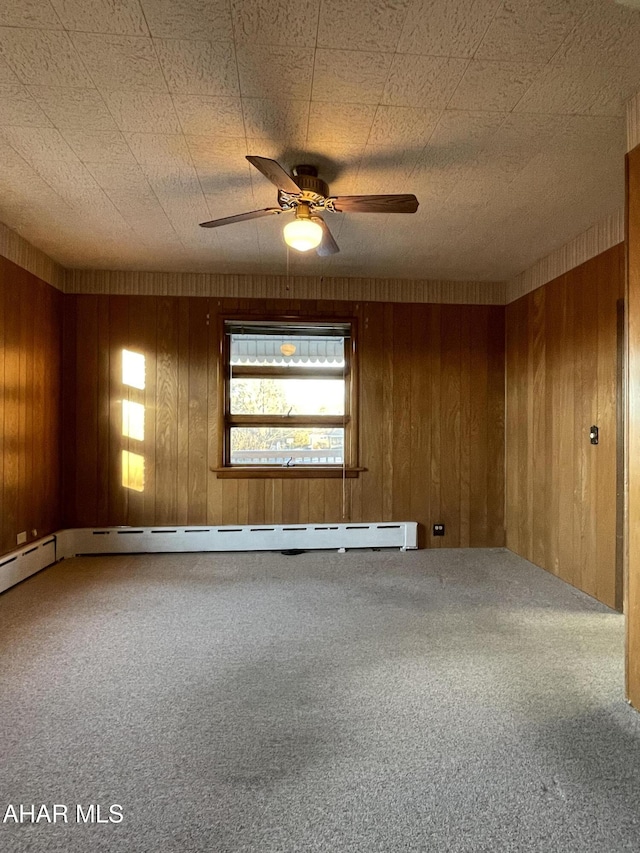 spare room featuring carpet, wooden walls, ceiling fan, and baseboard heating